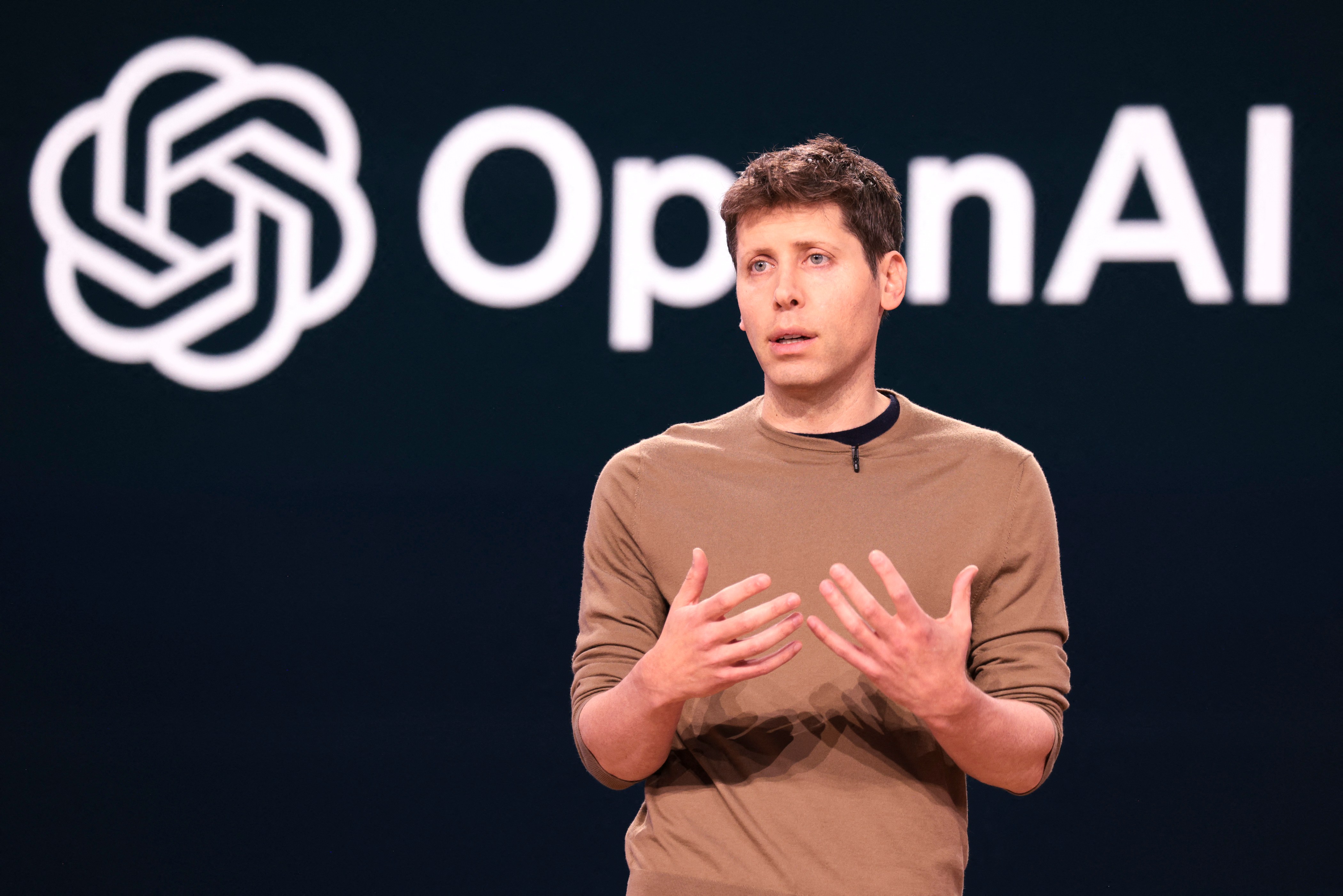Sam Altman ซีอีโอของ OpenAI ขึ้นพูดบนเวทีหน้าโลโก้ OpenAI ระหว่างงานเปิดตัวผลิตภัณฑ์