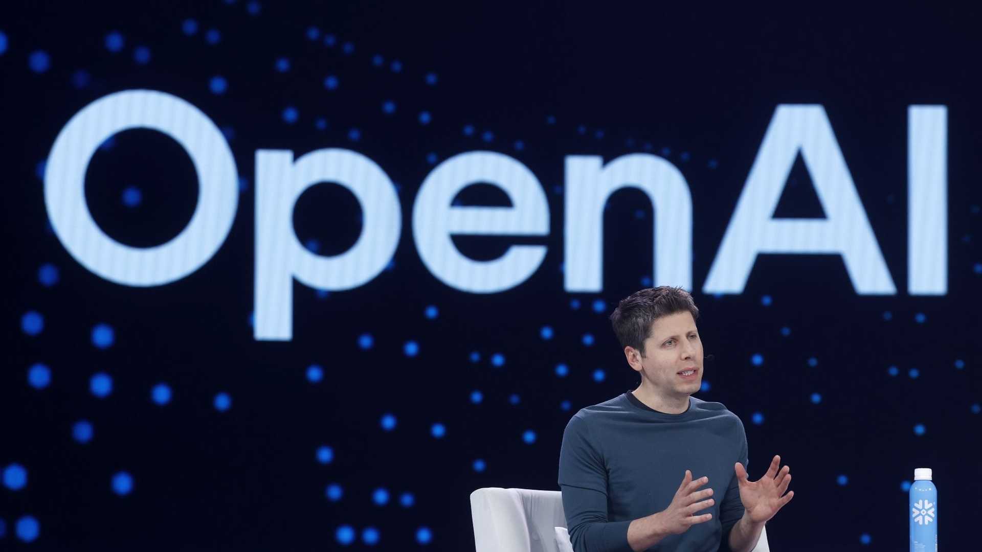 Sam Altman นั่งตอบคำถามบนเวทีมีโลโก้ OpenAI อยู่ด้านหลัง